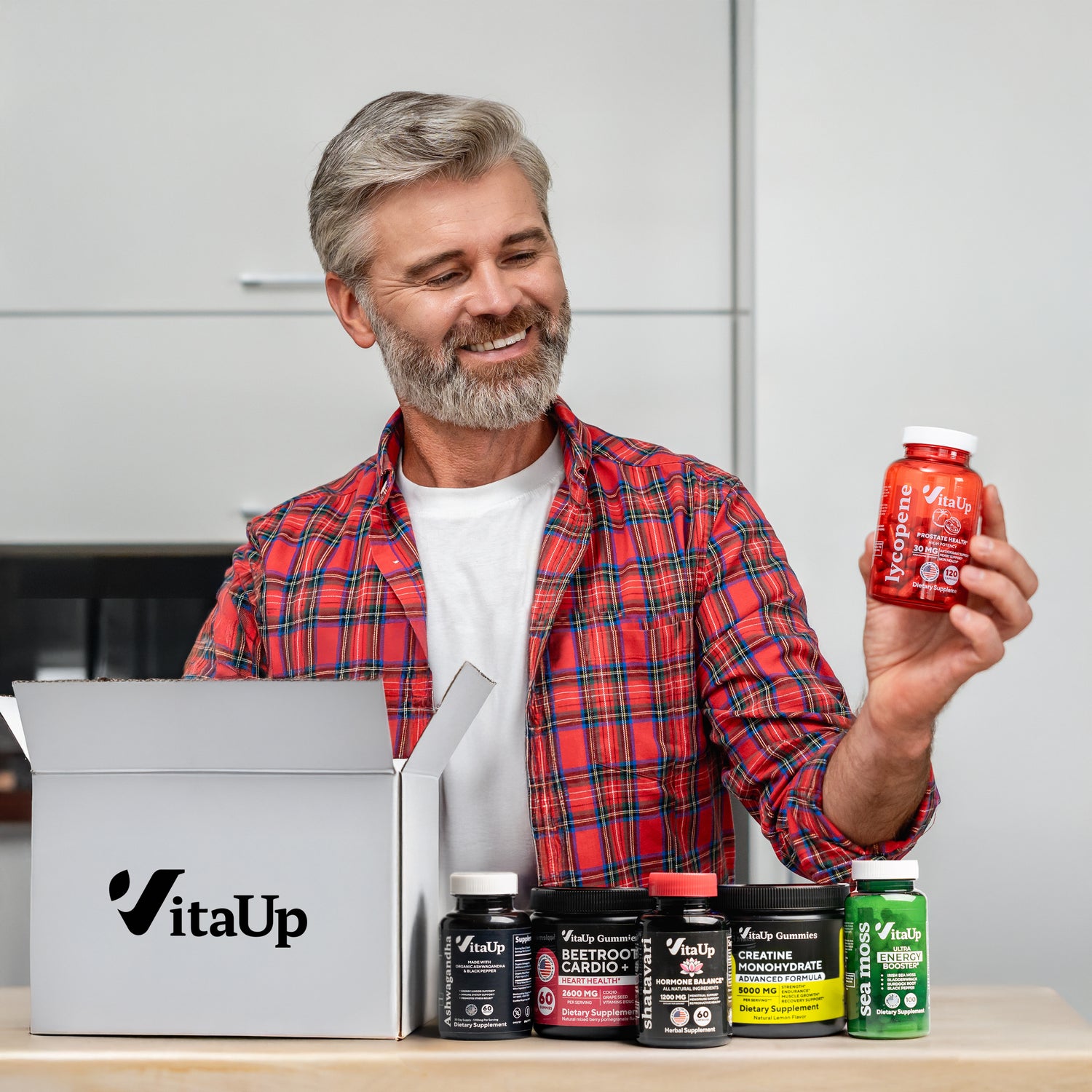 Smiling man holding a branded VitaUp box surrounded by six different VitaUp supplement products, promoting subscription savings and daily wellness support.