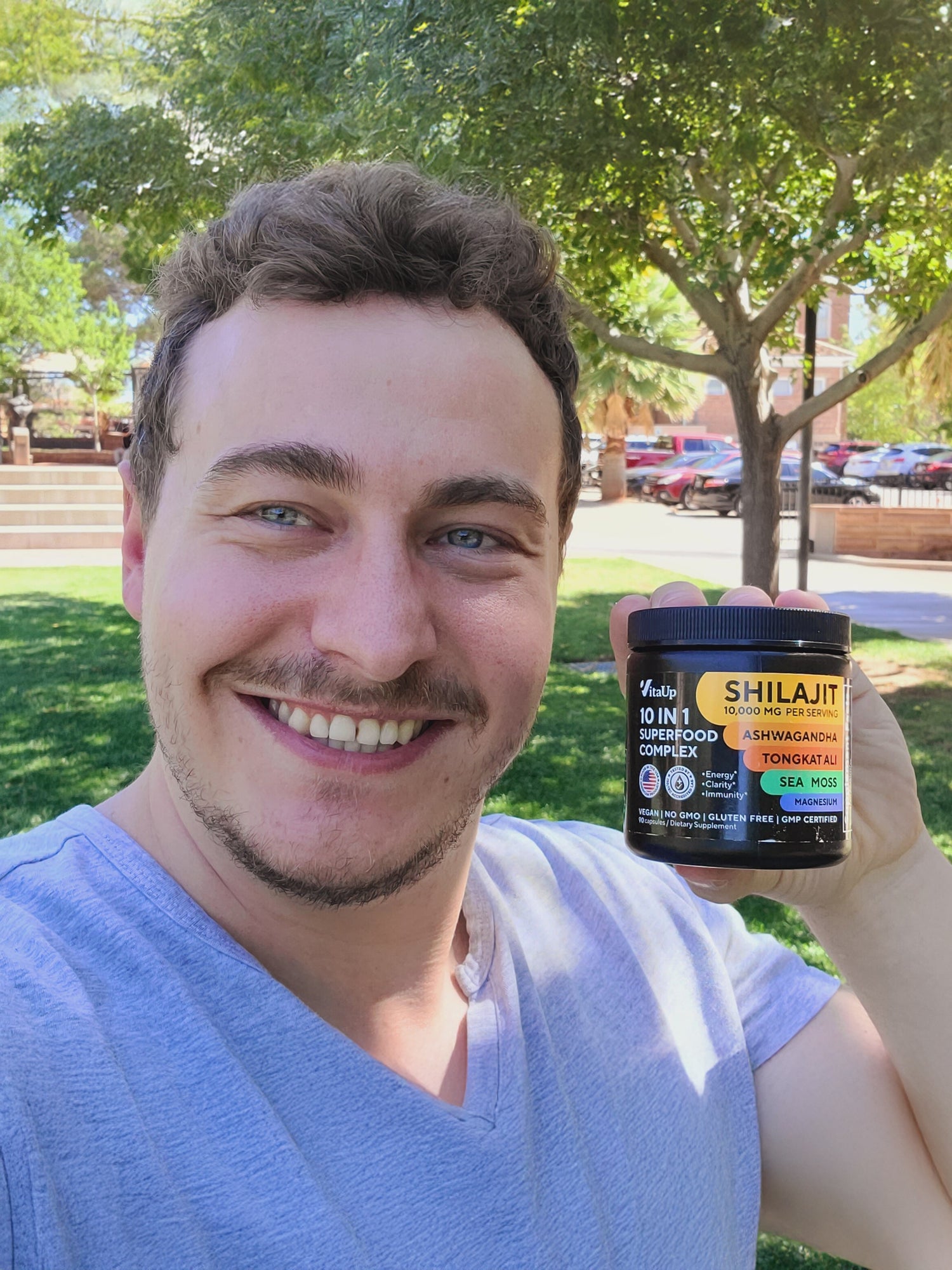 Smiling man outdoors holding VitaUp Complex Shilajit supplement jar, showing satisfaction with the product.