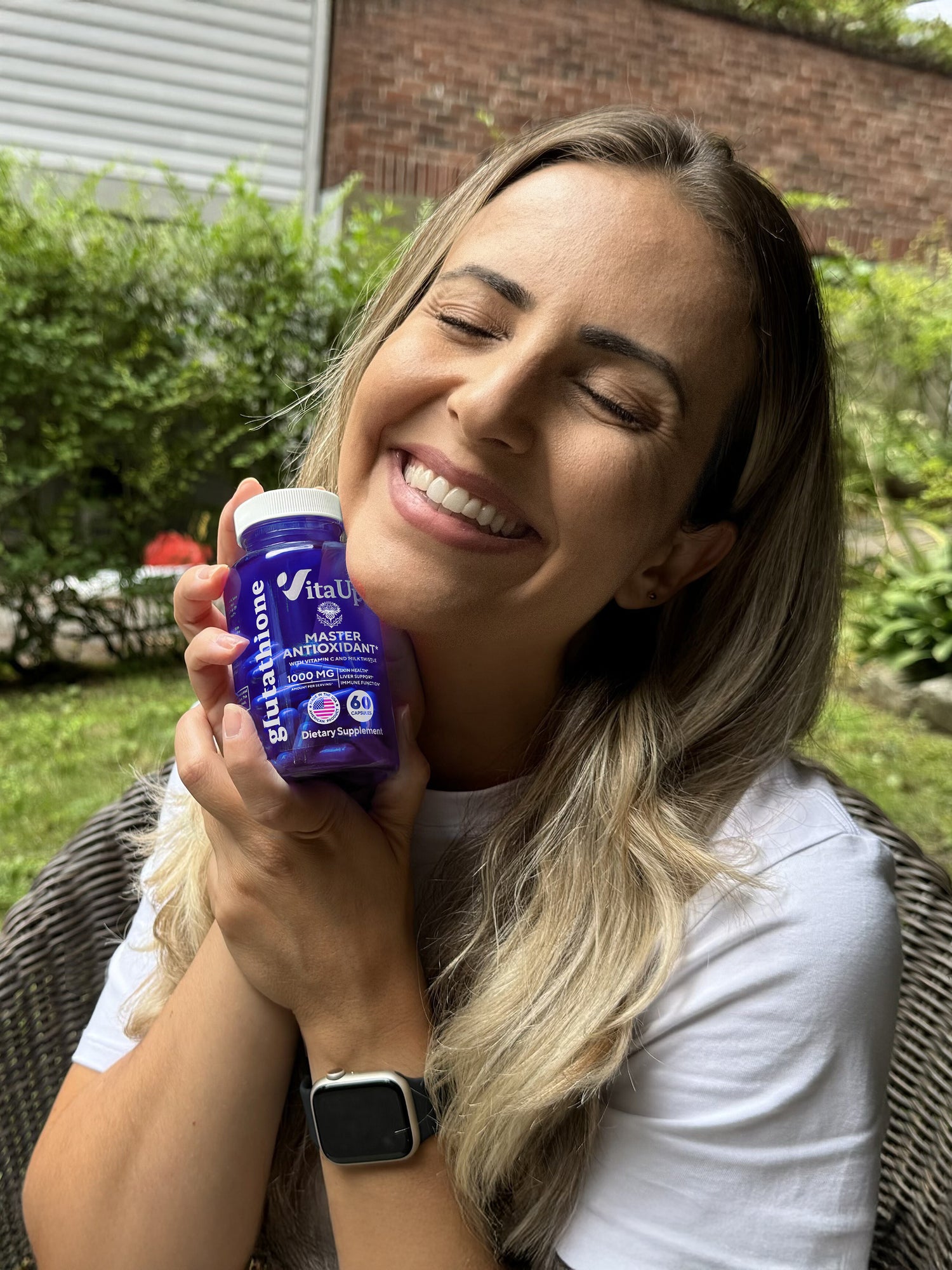 Woman smiling and holding a bottle of VitaUp Glutathione supplement, showcasing satisfaction and product confidence.