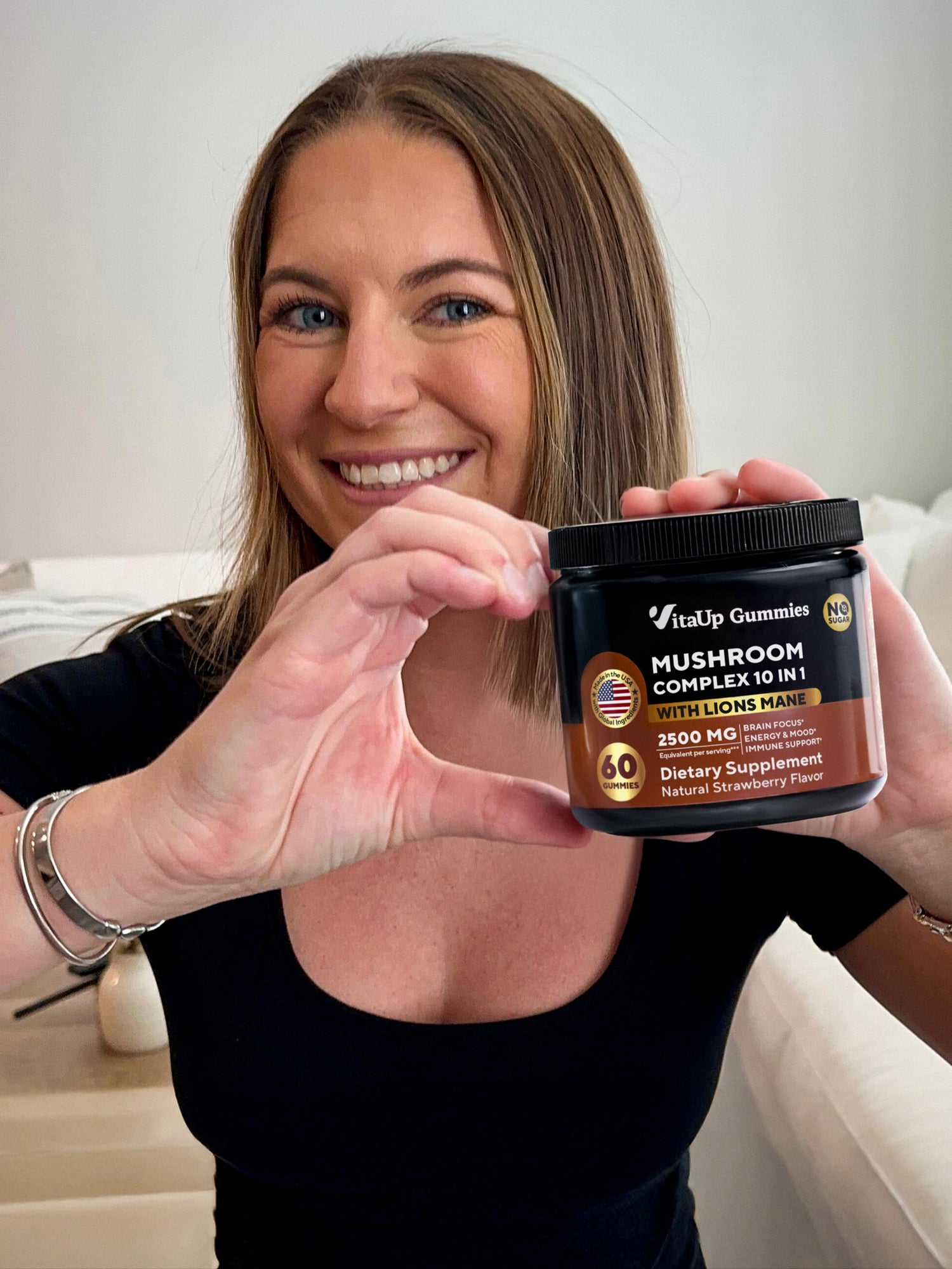 Smiling woman holding a jar of VitaUp Mushroom Complex 10-in-1 Gummies, showcasing product for brain and immune support.