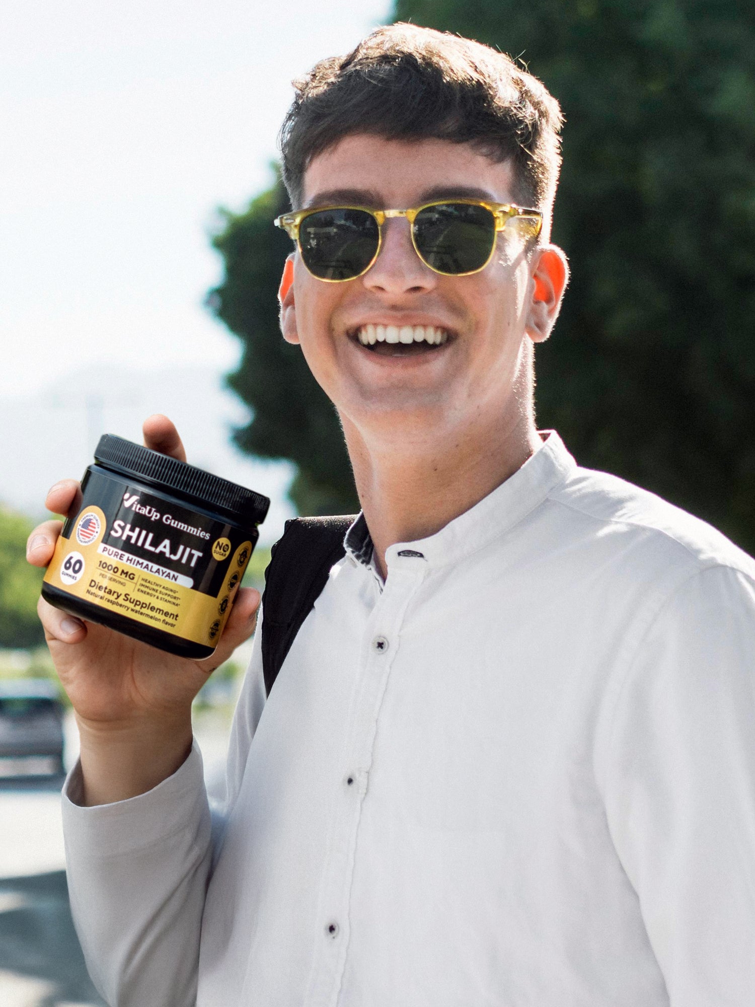 Young man holding a jar of VitaUp Shilajit Gummies, smiling outdoors, showing satisfaction with the product.